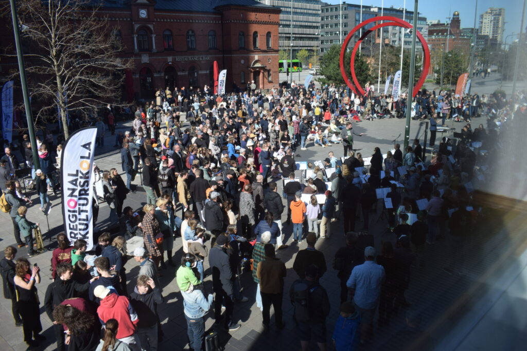 Stor folksamling på stadens torg i soligt väder.